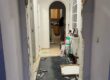 Imagen profesional en tonos azul oscuro y gris, con una puerta de vivienda parcialmente abierta, luz entrando desde el exterior y una balanza de justicia en primer plano. Estilo sobrio y corporativo. Texto: “Registro policial en domicilio · Defensa penal